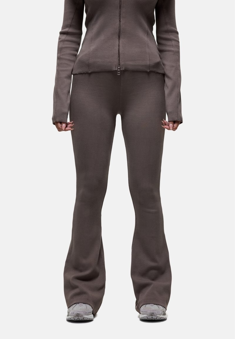Ensemble en deux pièces marron à côtes comprenant une veste zippée et un legging évasé, avec une finition texturée. Porté avec des baskets grises.