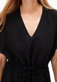 Czarna sukienka typu v-neck z krótkimi rękawami i elastyczną talią, z detalem w postaci sznureczka oraz teksturowanym materiałem.