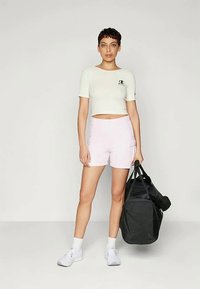 Ανοιχτό γκρι cropped t-shirt με λογότυπο, ροζ αθλητικά σορτς με τσέπες, και λευκές κάλτσες. Μαύρη μίνι τσάντα κρατημένη στο δεξί χέρι. Λείες υφές.