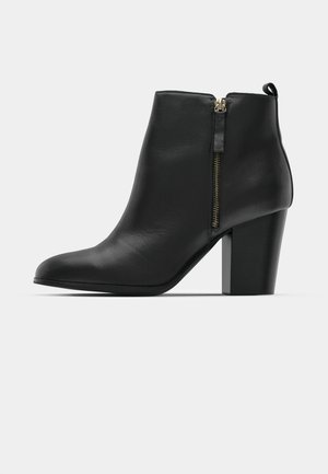 Schwarze Lederstiefelette mit glatter Textur, spitzer Zehe, seitlichem Reißverschluss und dickem Blockabsatz.