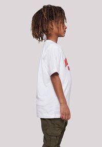 White cotton t-shirt featuring red graphic text on the front, paired with olive green cargo pants. Side view shows relaxed fit and short sleeves.