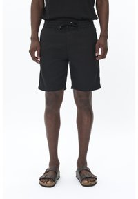 Black shorts made from lightweight fabric, featuring an elastic waistband with drawstring and side pockets. Worn with brown sandals.