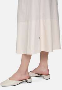 Biała bawełniana sukienka midi z lekko rozszerzanym dołem i czarnym akcentem w postaci guzika; zestawiona z beżowymi klapkami na kwadratowym nosku i słupkowymi obcasami.