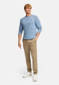 Lys blå strikket genser med rund hals, kombinert med beige chinos og hvite sneakers. Har ribbestrikkede mansjetter og en liten logo.