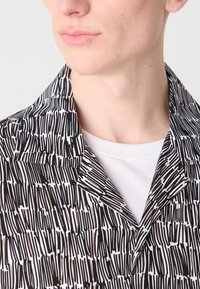 Short-sleeve shirt made of lightweight fabric featuring a black-and-white abstract pattern, with a collar and a white undershirt visible underneath.