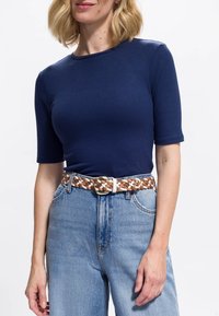 Marineblaues, geripptes T-Shirt mit kurzen Ärmeln, kombiniert mit hellblauen, hoch taillierten Jeans und einem geflochtenen braun-weißen Gürtel mit goldener Schnalle.