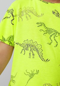Neon-grünes Baumwoll-T-Shirt mit Dinosaurier-Skelett-Drucken in dunkelgrün, kurzen Ärmeln und einem gerundeten Ausschnitt.