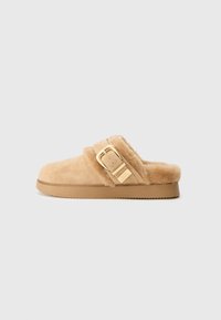 Zlatne suknje slip-on papuče od antilopa s mekim podstavom i velikim zlatnim kopčom s bočne strane, ravni potplat, izolirano na svijetlosivoj pozadini.