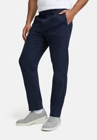 Pantaloni blu navy con una texture di tessuto liscia, dotati di tasche frontali e design a gamba dritta, abbinati a sneakers grigio chiaro.