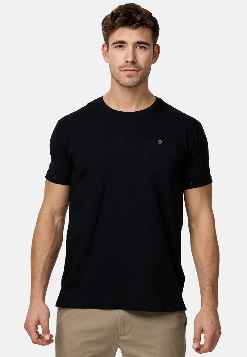 Schwarzes Kurzarm-T-Shirt mit rundem Ausschnitt, einer Tasche auf der linken Brust und einem kleinen runden Akzentknopf. Glatte Baumwolltextur.