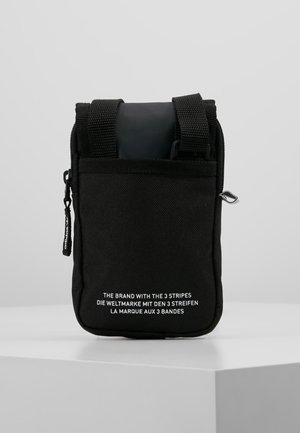 Petit sac bandoulière vertical noir avec des bretelles réglables et un texte blanc multilingue sur le devant, posé sur une surface blanche.