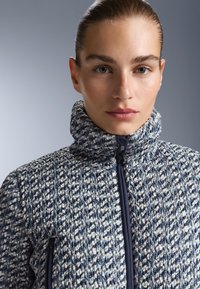 Tekstura se, uzorak jakne s visokim ovratnikom. Najvećim dijelom tamnoplava s bijelim naglascima. Prednji zip i bočne džepove.