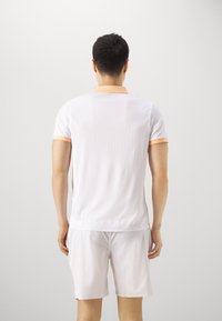 Polo à manches courtes blanc avec de légères rayures verticales, col orange et accents de manches assortis, accompagné d'un short léger.