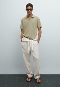 Světle zelená polo triko, volné béžové lněné kalhoty a černé žabky. Sluneční brýle dokončují ležérní, letní outfit.