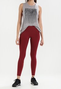Top grigio senza maniche con un design grafico nero, abbinato a leggings borgogna attillati e scarpe da ginnastica nere. Tessuto liscio, vestibilità comoda.