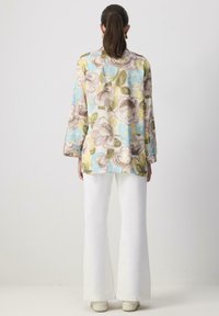 Floral blouse in pastel shades of blue, yellow, and brown, with long sleeves and a loose fit. Paired with white flared pants.