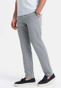 Harmaat housut, joissa on muotoiltu malli ja jotka on valmistettu sileästä kankaasta. Sisältää sivutaskut ja ne on paritettu tummansinisillä liukkulahkeilla kengillä.