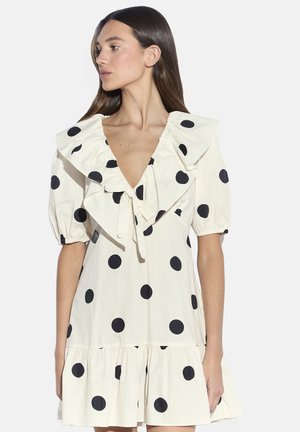 Vestito bianco con grandi pois neri, scollo e maniche arricciate, corto, con corpetto aderente e gonna svasata.