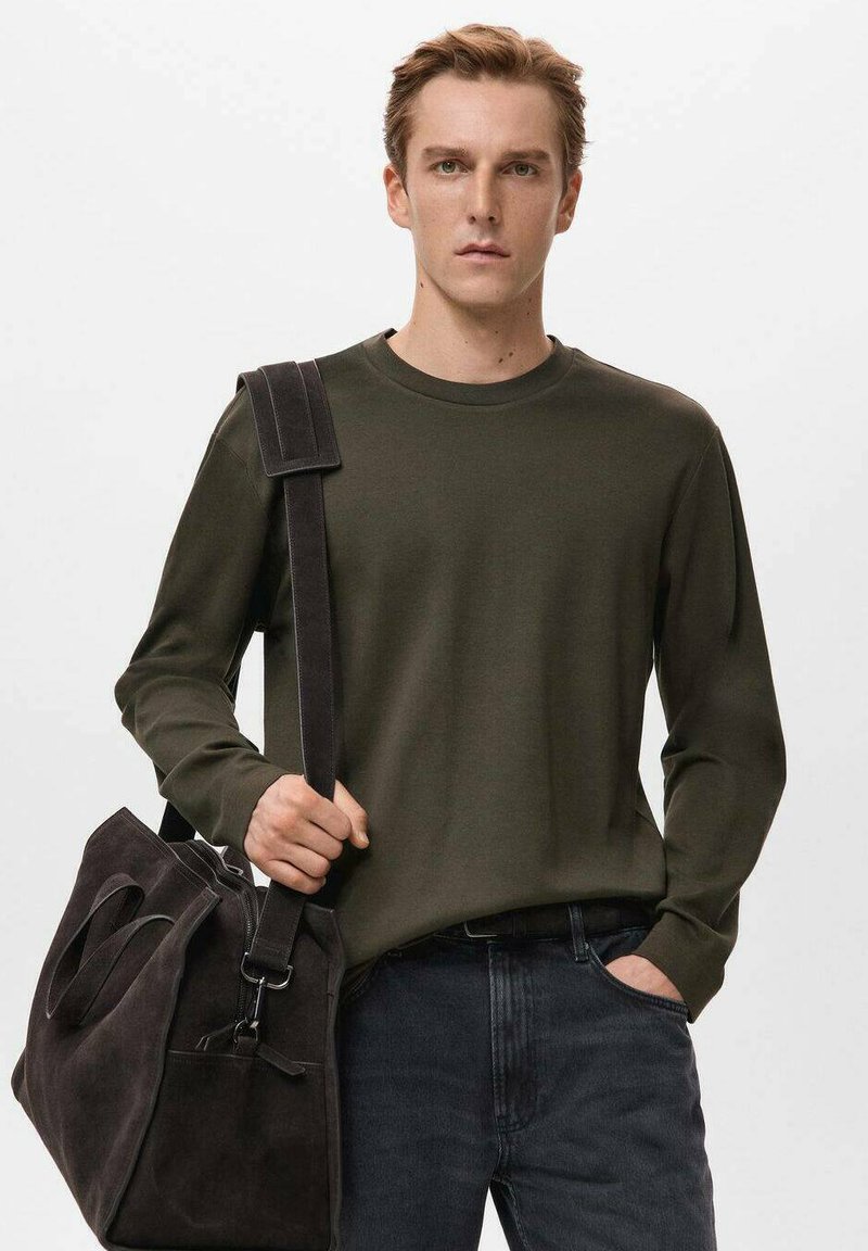 Donkergroen shirt met lange mouwen van gladde stof, gecombineerd met een zachte, donkergrijze suède tas, voorzien van stevige handvatten en een schouderriem.