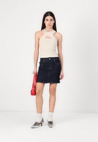 Beige geribbelde tanktop met een uitsnijd ontwerp, gecombineerd met een donkere denim minirok. Zilveren puntige schoenen en een rode handtas maken de look compleet.
