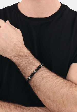 Bracciale nero con perline che presentano una combinazione di perline nere opache e lucide, decorate con perline d'accento argentate, indossato su un polso con peli visibili.