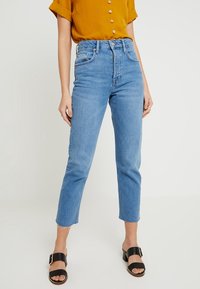 Vaaleansinisen denimikankaan farkut, joissa on korkea vyötärö, suora lahje ja risat helmat. Yhdistetty sinapinkeltaiseen nappipaitaan ja mustiin sandaaleihin.