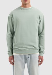 Light green crewneck sweatshirt with long sleeves, ribbed neckline and cuffs, paired with light blue jeans. Soft texture, relaxed fit.