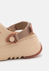 Beige plattform sandalett med justerbart tygband och triangulär plastspänne, med en strukturerad sula och gummiklack.