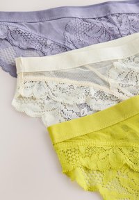 Trois culottes pour femmes avec bordure en dentelle en lilas, crème et jaune, superposées sur une surface blanche.