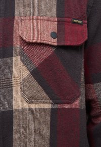 Flanellhemd mit kariertem Muster in Rottönen, Braun und Schwarz. Verfügt über eine Brusttasche und eine strukturierte Stoffoberfläche.