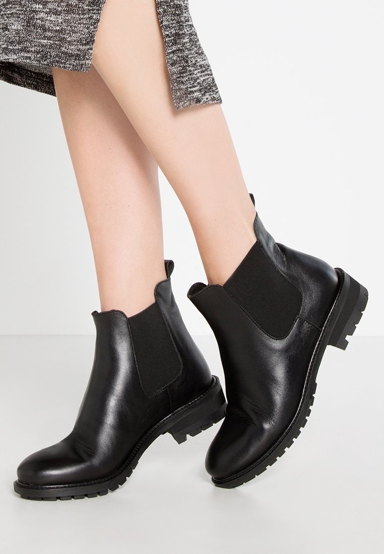 Czarne skórzane botki za kostkę z elastycznymi panelami bocznymi, zaokrąglonym noskiem i gumową podeszwą, oferujące fakturowany wzór na cholewce.