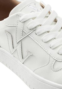 Baskets blanches en cuir avec des accents texturés, un logo visible, un design de lacets à plat et une semelle en caoutchouc striée. Surface lisse avec des détails de couture.
