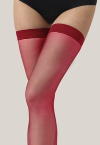 Rote, oberschenkelhohe Strümpfe mit transparenter Textur, die oben ein festes rotes Band und ein glattes Aussehen aufweisen und bis zur Mitte des Oberschenkels reichen.
