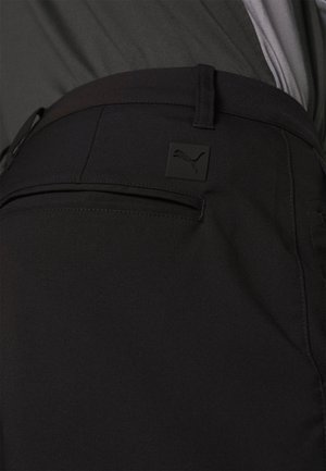 Black athletic pants with a smooth texture, featuring a back pocket and a small black Puma logo patch on the waistband.