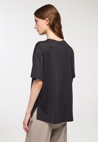 T-shirt nera in cotone dalla vestibilità comoda, con maniche corte, scollo rotondo e spacchi laterali, caratterizzata da una texture liscia e un design semplice.