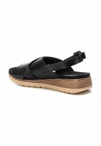Sandal in pelle nera con design a tracolla incrociata, soletta imbottita e suola in gomma testurizzata con accenti marroni sovrapposti. Include una strap regolabile.