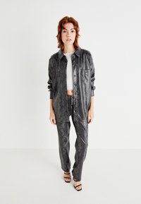 Grau Kunstleder-Outfit mit einem Schlangenhautmuster, bestehend aus einem Hemd mit Knöpfen und passenden Hosen, kombiniert mit schwarzen Sandalen mit Riemen.