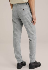 Pelēkās svītrainās bikses, izgatavotas no teksturēta auduma, ar pielāgotu piegriezumu, ar aizmugures kabatu, kas aizdarīta ar brūnu pogu, valkātas kopā ar melnām svinīgām kurpēm.