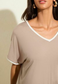 Beige V-hals T-shirt met een contrasterende witte rand, gemaakt van gladde stof, met korte mouwen en een relaxte pasvorm.