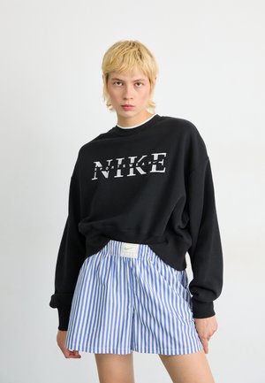 Zwarte Nike-hoodie met groot wit logo, gecombineerd met blauw-witte gestreepte shorts met een Nike-label aan de taille. Korte mouwen.