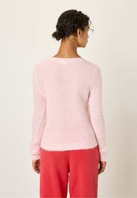 Pull en peluche rose à manches longues et décolleté large, avec des poignets côtelés. Associé à un pantalon rouge ample. Design simple.