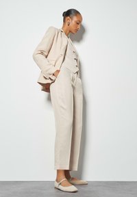 Beige linen suit featuring a tailored blazer, fitted vest with buttons, and wide-leg trousers, paired with matching slip-on shoes.