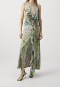 Lång halterneck-klänning i lätt grön och blommönstrad tyg, med djup urringning och utsmyckad midjedetalj.