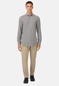 Camicia abbottonata a maniche lunghe grigia con righe verticali, abbinata a pantaloni beghè e sneakers nere. Colletto ben definito e bottoni frontali.