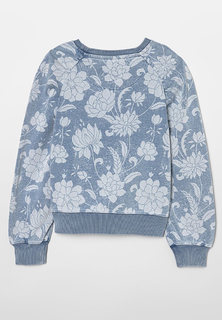 Sweatshirt bleu à motifs floraux texturés, avec des manches longues, des poignets côtelés et un col rond. Des fleurs de couleur claire se détachent sur fond bleu.