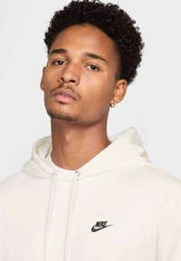 Felpa crema realizzata in morbido tessuto con cappuccio regolabile, con il logo Nike nero sul petto e una finitura texture sottile.