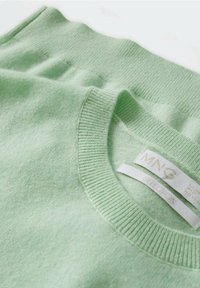Pull tricoté vert clair doux avec col rond côtelé et étiquettes de marque blanches visibles à l'intérieur de l'encolure.
