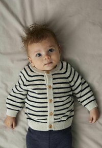 Vauvoille kudottu vaaleanbeige villatakki tummansinisillä raidoilla, jossa on nappikiinnitys ja puunapit, yhdistettynä teksturoituihin tummiin housuihin.