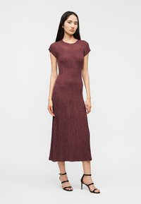 Φόρεμα μπορντό ριμπ πλεκτό με κοντά καπάκια, εφαρμοστή σιλουέτα και μήκος μέχρι τη μέση της γάμπας. Συνδυάζεται με μαύρες ψηλοτάκουνες πεδιλάκια με λουράκια.