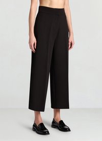 Pantalon noir à jambes larges avec une texture lisse, taille haute et sans attaches visibles, associé à des mocassins noirs.